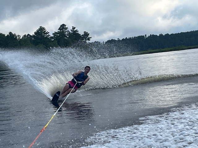 photo of young man waterskiing on one ski with a large spray of water next to him as he turns.