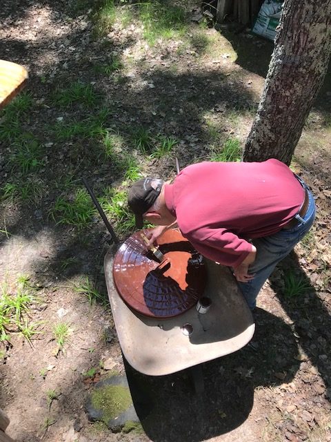 Photo of man sealing a cover for an outdoor fire pit with a paintbrush and sealer.