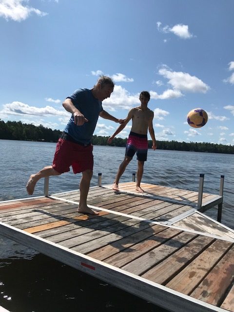 photo of two boys on the pier about to hit a soccer ball that is mid air.