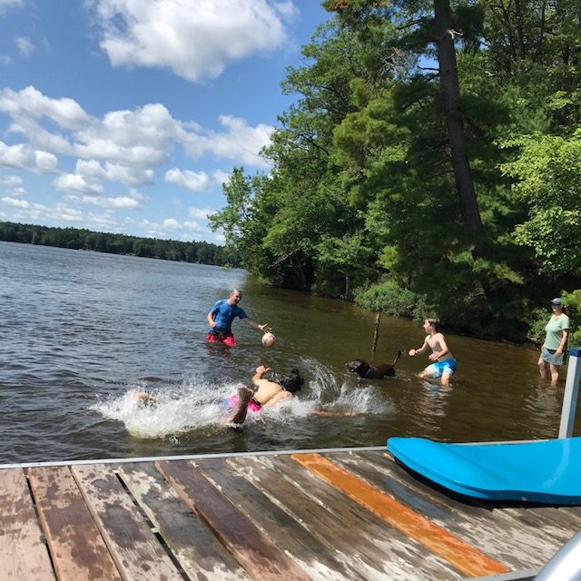 Photo of three boys playing "water soccer" in the lake by a pier with Rey the dog.