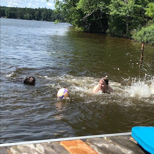 photo of boy and dog in a lake swimming towards the soccer ball.