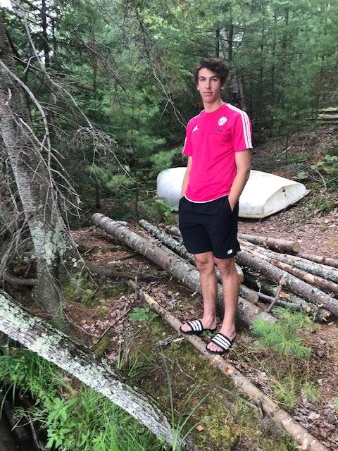 photo of young man, standing on land next to logs for the project.