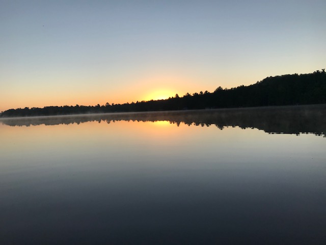 photo of sunrise on a calm lake with some mist by the shoreline in the distance.