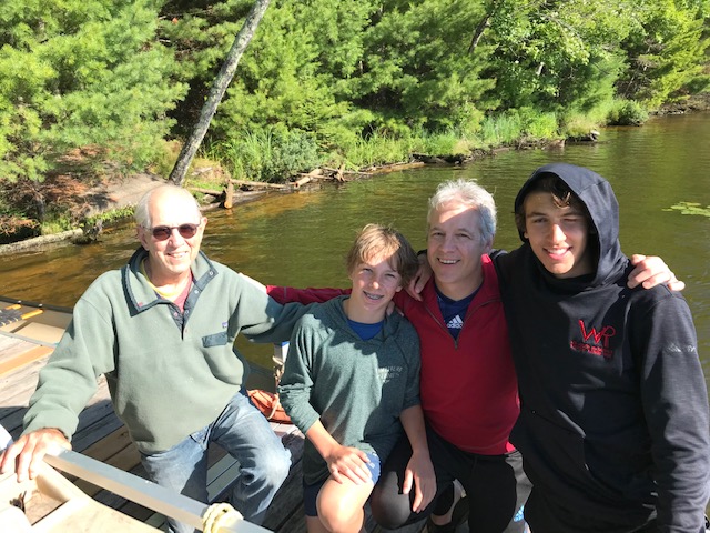 Two men and two boys posing fro a photo at the lake.