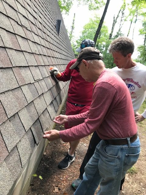 Three men looking at shingles on an a-frame roof.