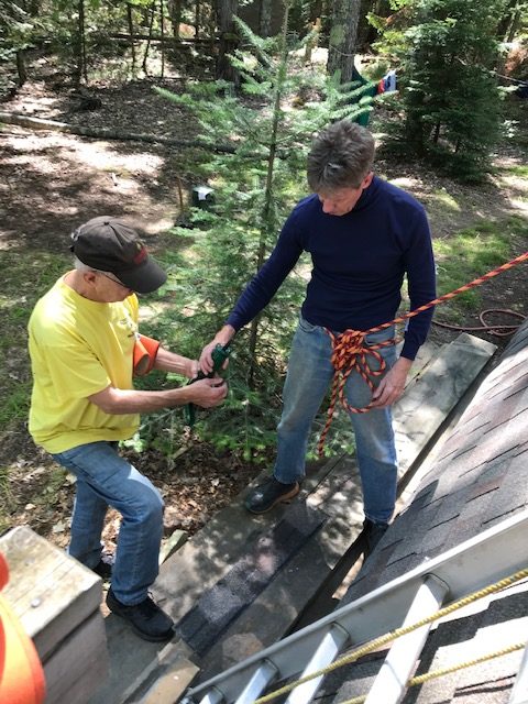 Man getting ready to get on a ladder.  Another man is double checking the harness for safety.