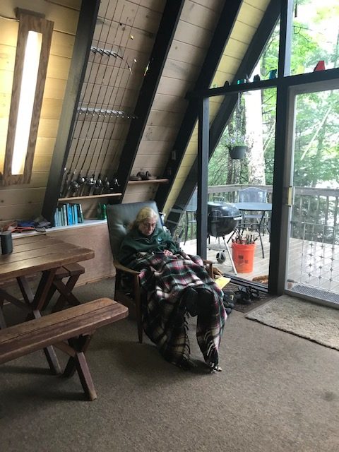 photo of older woman reading in a cozy chair with a plaid blanket over her legs.