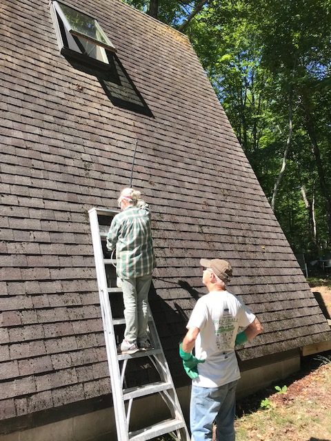 photo of a woman on a ladder on the roof and man looking on.