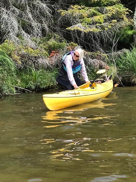 photo of woman getting into a kayak next to the lake shore near trees.