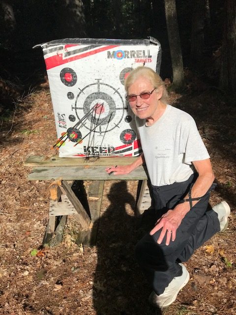 photo of older woman knelling in front of archery target with her arrows in it.