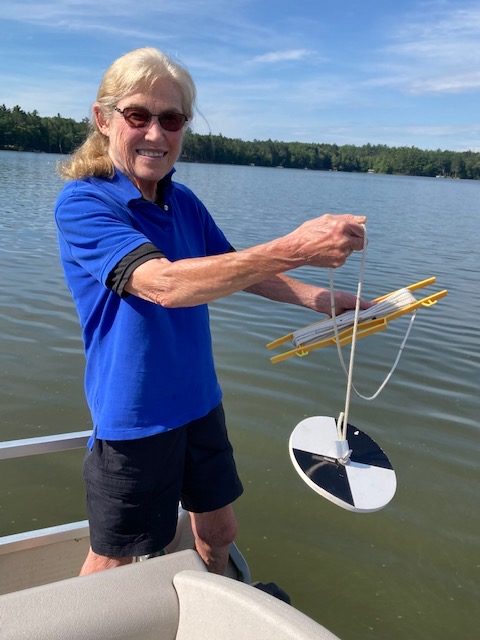 Photo of woman holding a clarity measurement tool for water that has a white and black disk.