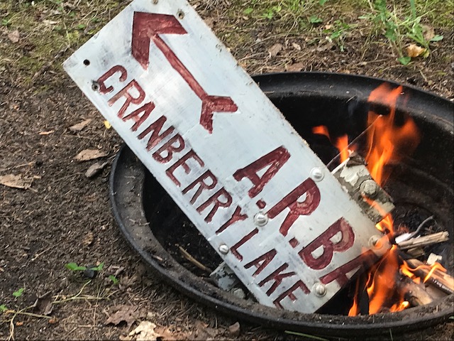 photo of pit fire with a piece of board with writing on it.