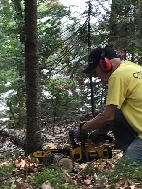 man sawing a log wearing a baseball hat and earmuffs to reduce sound