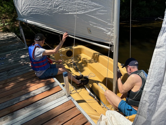 two men putting up sail in sailboat while docked